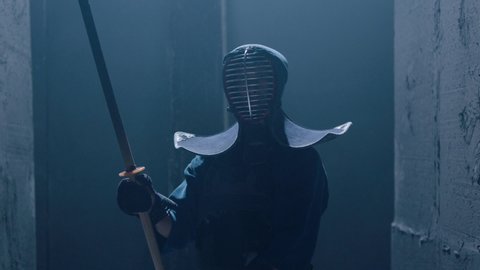 Portrait of a Japanese kendo fighter hold a burning sword . Epic Kendo warrior stands in armor in the fog and looking at the camera with his fire shinai . Mysterious video scene . Shot on Arri Alexa .
