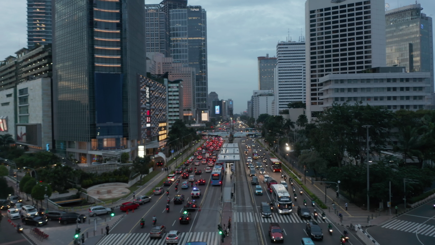 Low flying aerial view of busy multi lane road with car traffic near roundabout in the evening with beautiful city lights glowing in downtown Jakarta, Indonesia  Royalty-Free Stock Footage #1065473866