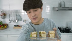 Happy cheerful Asian man using smartphone selfie live streaming while cooking sandwich breakfast in kitchen. Healthy lifestyle 