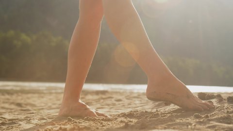 Close-up: women's feet playing with sand on the beach. Slender legs of a young girl in the sand, the foot moves from side to side, tossing the sand. Sunny day, the concept of leisure. Slow motion, 4K