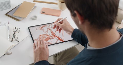 Lviv, Ukraine - May 28, 2020: Male web designer creating sketch of illustration on digital tablet.Talanted man using pad and stylus while sitting and working on project at his desk.
