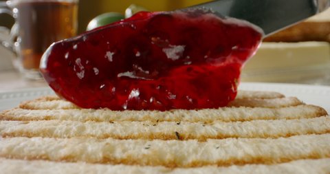 Knife spreading berry jam on piece of toast. Preparation of sweet yummy sandwich - food and drink close up 4k footage