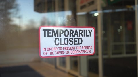 Cafe owner hangs "Temporarily closed" sign on glass door during pandemic covid-19 coronavirus quarantine. Business suffered financial losses.