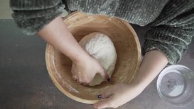 Aerial view video of a woman wearing green jumper kneading a pizza dough on a wooden bowl. 