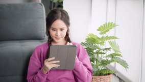 Asian young girl starting a video call on tablet talking having conversation with people, online social interaction social media communication, at home happy joyful in living room modern lifestyle.
