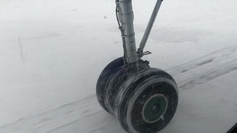 Airplane landing gear before takeoff. The plane is rolling on a snow-covered airfield. View from the porthole.
