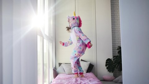 Little girl in kigurumi dancing in unicorn pajamas.