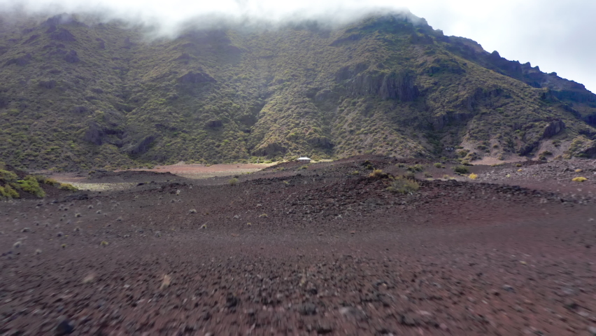 Drone flying fast over the volcanic land and crater landscape to rustic cabin in Haleakala National Park, Maui, Hawaii, USA. Outdoors adventure and nature travel. Old building in ancient volcanic peak