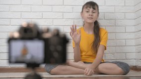 Speak about yoga on video. A young child record her vlog on camera in the room.
