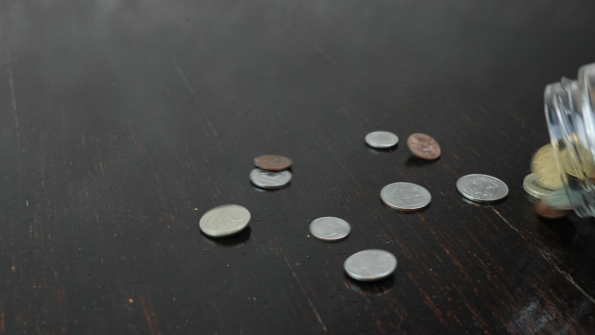 Stack of coins are falling on table from glass jar moneybox. Money coins are pouring on black background. Saving money concept. Concept of poverty and financial crisis. Falling of world economy, a Business & Finance Video by CreatorRuslanMikaielian