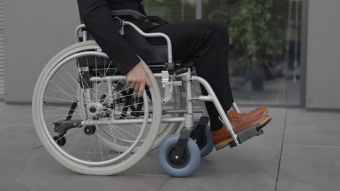 Crop view of disabled male person in stylish outfit going on wheel chair at street. Side view of successful male person riding to work near office building. Concept of motivation, grid