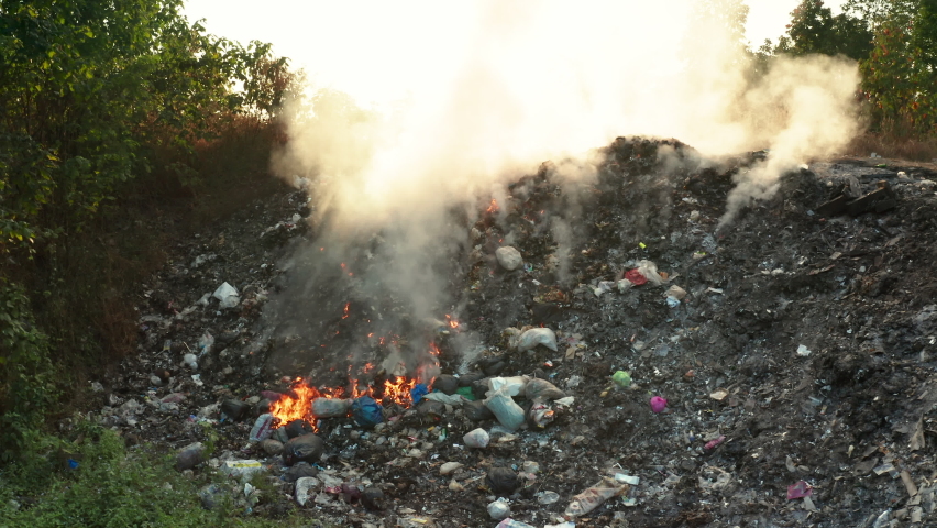 Garbage and fire burn in landfill. Also call trash, waste, rubbish. Destruction with combustion, heat, flame. Occurs smoke, toxic cause of air pollution, environmental damage and global warming. Royalty-Free Stock Footage #1065530206