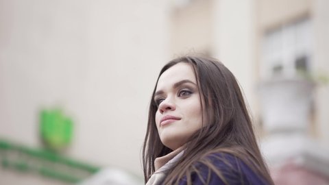 Young girl from a pensive look. Close-up with blurred background. The girl is waiting for the young guy and turns her head around in search of her lover. A gentle smile. Girl with dark hair 