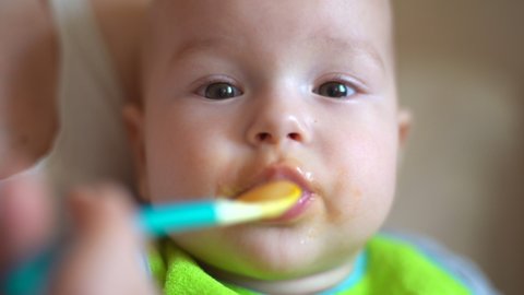 Mother Feeds Baby From Spoon with Pureed Food. Close-up of a Kid Eating Porridge.