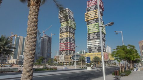 DOHA, QATAR - CIRCA FEB 2019: Doha skyline timelapse hyperlapse with colorful Al Marina Twin Towers building located the Lusail area of the capital of Qatar. Palms and trees. Traffic on the road