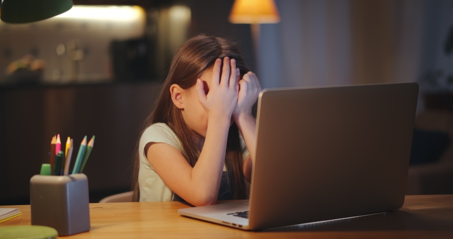 Tired preteen girl rubbing eyes sitting at table with computer studying online late in evening. Exhausted pupil having online class on laptop sitting in dark living room | Shutterstock HD Video #1065536488