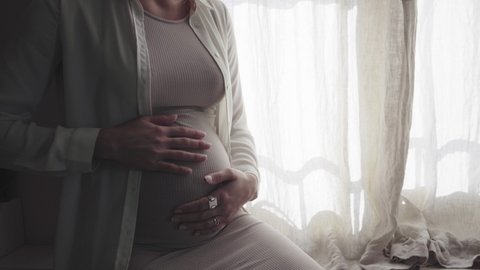 Pregnant woman stroking baby belly at window