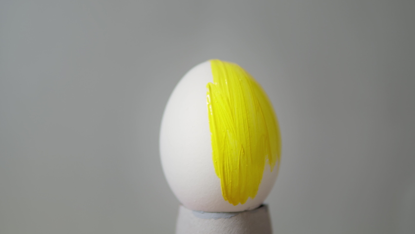 Easter egg on a gray background. Painting in yellow. Easter in Pantone color 2021. Decorating Easter eggs with trendy colors, close-up. Easter concept. Yellow egg on a gray background. Royalty-Free Stock Footage #1065539101