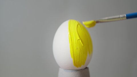 Easter egg on a gray background. Painting in yellow. Easter in Pantone color 2021. Decorating Easter eggs with trendy colors, close-up. Easter concept. Yellow egg on a gray background.