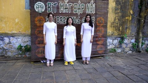Hoi An, Vietnam - june 05, 2020 : Three vietnamese young girls dancing near the wall on the street in the old town Hoi An, Vietnam