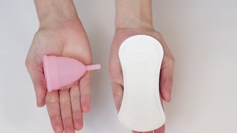 Young woman hands holding sanitary pad and reusable pink silicone menstrual cup.
