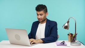 Shocked unshaven man closing eyes with hand watching awful disgusting video on laptop, dont want to look at that. Indoor studio shot isolated on blue background