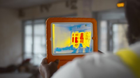 Close up of african builder analyzing heat on wall with thermal imaging camera app on tablet. Construction worker using infrared camera on digital tablet in renovating apartment