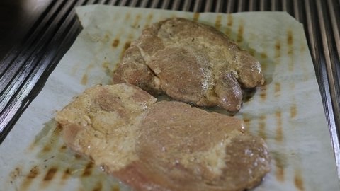 Close-up of two steaks being grilled on baking paper in a professional restaurant kitchen.