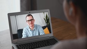 Above shoulder view on virtual meeting on a laptop screen. Smiling male online teacher, distance tutor or employee talking with female, video call conference on a computer