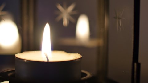 hygge concept: close up view footage of igniting a candle in the dark, candle position on the left of the frame. Cozy home interior decor, burning candles, burning candles on the dark background.