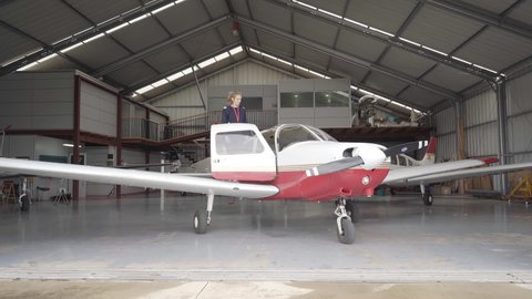 A flight instructor in the hangar entering her plane and closing the doors, preparing to fly.