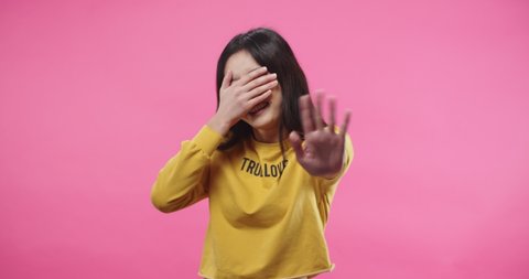 Portrait of beautiful Asian young woman saying NO denying something, rejecting and covering face with hand don't want to watch while standing isolated on pink background in studio. Negative reaction