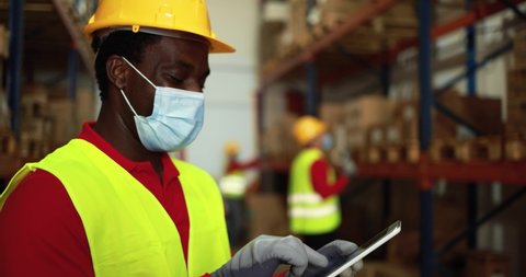 African worker using tablet inside warehouse while wearing safety  face mask for coronavirus prevention