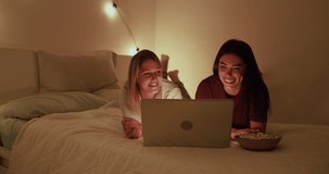 Young women watching movie on laptop at home inside bedroom - Pajama party and friendship concept