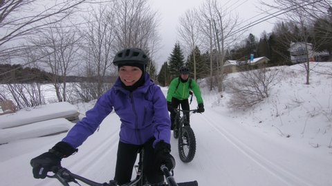 Fat bike in winter. Fat biker riding bicycle in the snow in winter. Selfie video by woman and couple living healthy outdoor active winter sports lifestyle.