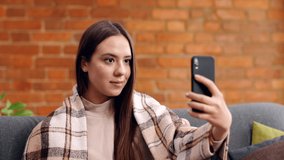 Video call and online communication. Close up portrait of young cheerful woman video chatting with friends, waving hand hello and talking at home, slow motion