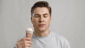 Tooth sensitivity. Young guy eating ice-cream cone and suffering from acute toothpain, grey studio background, close up portrait
