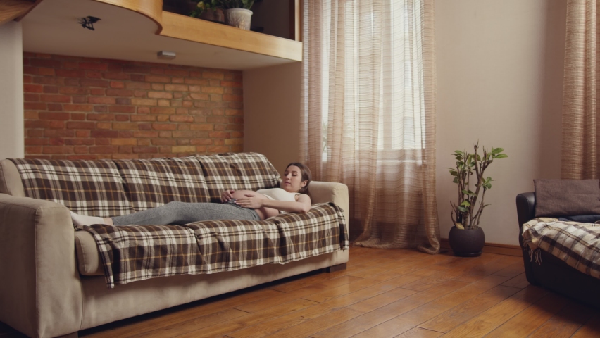 Young pregnant woman waking up from day nap, standing from sofa and going away, rest at home, slow motion