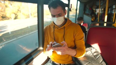 Masked man uses mobile phone during the bus trip. Buying an electronic ticket on road. Transportation passengers in city. Respect for wearing a mask in public place.