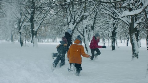 HANDHELD Group of kids having snowball fight brawl, running through the trees covered with snow. Fun winter games outside. 120 FPS slow motion shot