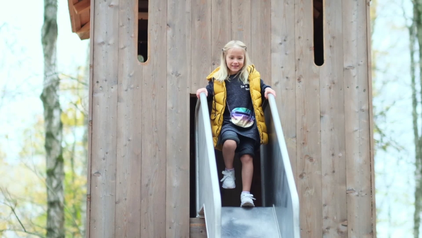 cute cheerful girl at the entrance to the treehouse dances and rolls down the slide