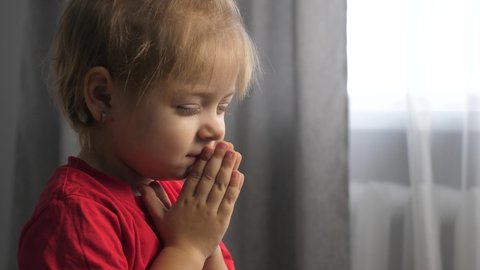 little daughter girl makes a wish prayers bedtime religion concept. prayer lifestyle child indoors praying by bed in front of window