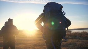 two tourists teamwork. with backpacks slow motion lifestyle walking go silhouette in the sunlight glare of the sun at sunset. two men hikers climb mountains overcoming difficulties concept teamwork - Powered by Shutterstock - Get 15% off with code: PIKWIZARD15