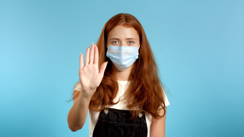 Pretty woman in protective mask disapproving with NO hand sign gesture. Denying, rejecting, disagree, portrait of beautiful girl or student on blue background | Shutterstock HD Video #1065588535