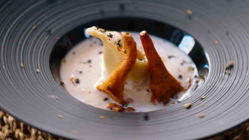 Close up view duck confit ravioli served portion with cream sauce and golden chanterelle mushroom on spinning black plate. Italian cuisine, restaurant main course dish, food in motion concept
