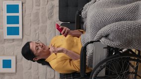 Elderly woman taking selfie with cell phone in a wheelchair.Elderly woman sitting at home in a wheelchair, taking selfie with her mobile phone.Video for the vertical story.