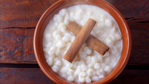 White corn cooked with milk known as canjica, canjicao or mungunza, typical dish of Brazilian gastronomy, in a rustic bowl, on wooden table