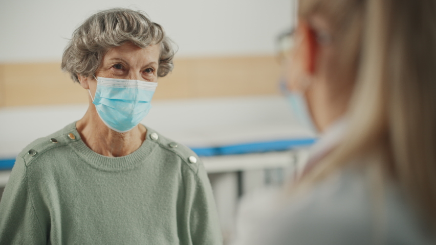 Female Family Doctor is Speaking to a Senior Woman During Consultation in a Health Clinic. Both are Wearing Face Masks. Physician in Lab Coat Prescribing Drugs to Elderly Patient in Hospital Office. | Shutterstock HD Video #1065599296