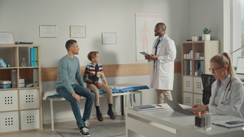 Father Visiting a Friendly Family Doctor with His Young Teenage Son Who Has Broken His Arm. They Talk to an African American Physician in a Hospital Office. Boy is Wearing an Arm Brace.