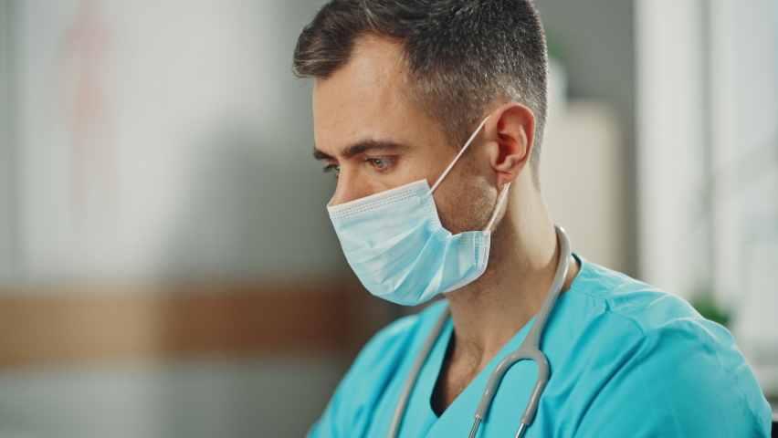 Portrait of Experienced Male Nurse Wearing Blue Uniform and Face Mask at Doctor's Office. Medical Health Care Professional Working On Battling Stereotypes to Gender Diversity in Nursing Career. | Shutterstock HD Video #1065599569